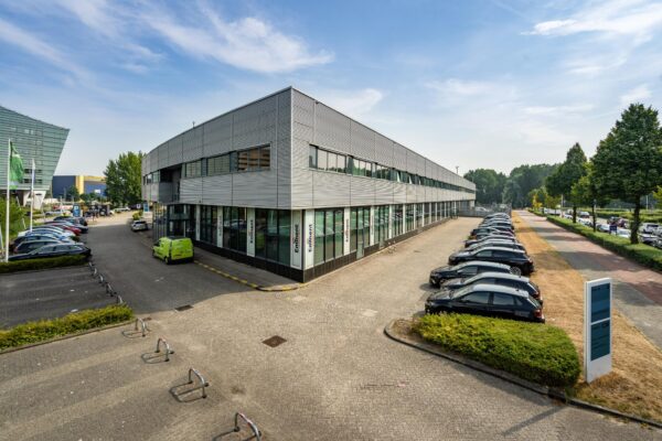 Kantoorgebouw aan de Rivium Boulevard met parkeerplaatsen en omliggende bedrijven op een zonnige dag.